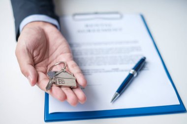 Kontrat belgelerini imzalarken elinde ev anahtarı tutan bir adam. Kontrat sözleşmesi, gayrimenkul, alım-satım ve sigorta kavramları