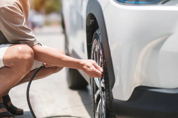 man driver hand inflating tires of vehicle, removing tire valve nitrogen cap for checking air pressure and filling air on car wheel at gas station. self service, maintenance and safety