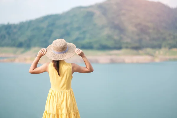 Asian Woman in yellow dress and hat Traveling at outdoor, Happy traveler looking to Khun dan Prakarnchon dam. landmark and popular for tourists attractions in Nakhon Nayok, Thailand