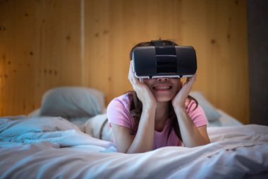 Yatakta sanal gerçeklik kulaklığı kullanan genç bir kadın. VR, gelecekteki dijital teknoloji, oyun, film eğlencesi, metaevren, NFT ve 3D siber uzay kavramı