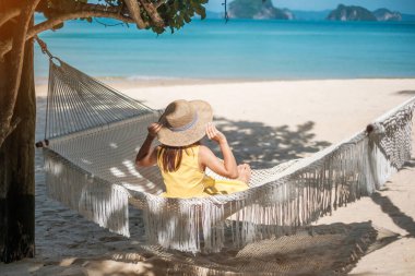 Mutlu Kadın Gezgin cennet kumsalındaki bir hamakta dinleniyor. Sarı elbiseli kadın turist tropik deniz kenarında dinleniyor. Tatil, seyahat, yaz, seyahat ve tatil konsepti.