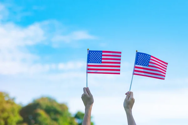 hand holding United States of America flag on blue sky background. USA holiday of Veterans, Memorial, Independence ( Fourth of July) and Labor Day concept
