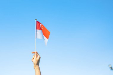 Mavi arka planda Singapur bayrağını tutan el. Singapur Ulusal Günü ve mutlu kutlamalar.