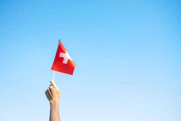 青い空を背景にスイス国旗を掲げている手 スイス国民の日と幸せなお祝いの概念 — ストック写真