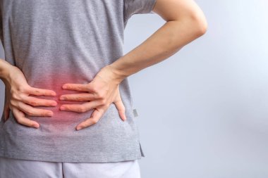 Gri arka planda kas ağrısı olan yetişkin bir kadın. Piriforis Sendromu, bel ağrısı ve omurga baskısı nedeniyle sırt ağrısı çeken yaşlı bir kadın. Ofis sendromu ve tıbbi konsept