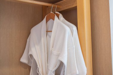 White clean bathrobe hanging in wooden wardrobe at luxury hotel or home. Relax and travel concept