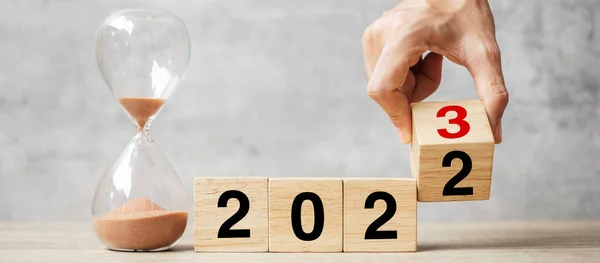 hand flipping block 2022 to 2023 text with hourglass on table. Resolution, time, plan, goal, motivation, reboot, countdown  and New Year holiday concepts