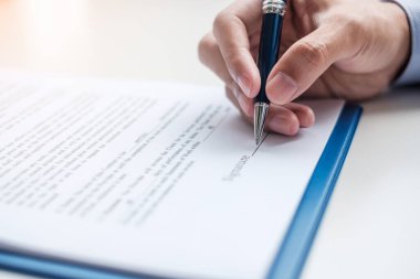 İş adamı okuduktan sonra sözleşmeyi imzalıyor, elinde kalem tutuyor ve iş raporunu onaylıyor. Anlaşma, ortaklık ve anlaşma kavramları