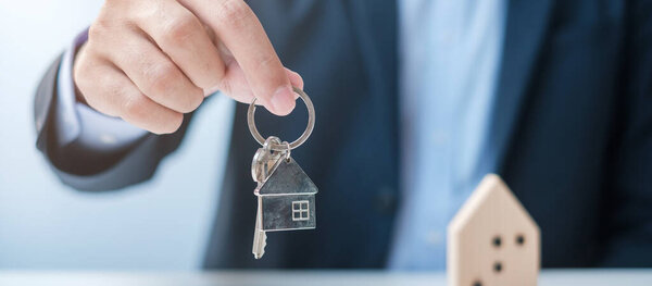 Businessman hand holding key with wooden Home model. Real estate, buy and sale, Property insurance, rental and contract agreement concepts