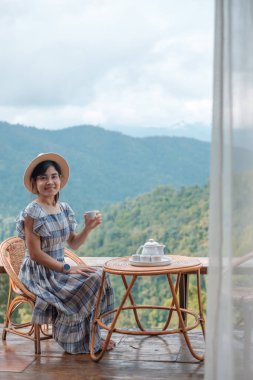 woman drinking tea and looking mountain view, young blogger stay at countryside homestay in the morning.Travel, vacation, journey, trip and relaxing concept