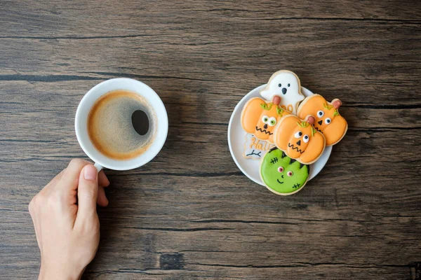 hand holding coffee cup during eating funny Halloween Cookies. Happy Halloween day, Trick or Threat, Hello October, fall autumn, Traditional, party and holiday concept