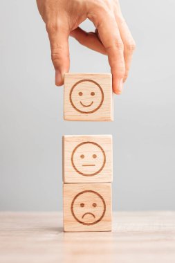 Elele tutuşan bir adam yüz bloğu. Müşteri, kullanıcı değerlendirmeleri için Emoticon 'u seçer. Hizmet derecesi, sıralama, müşteri değerlendirmesi, memnuniyet, değerlendirme ve geri bildirim kavramı