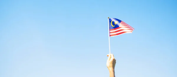 hand holding Malaysia flag on blue sky background. September Malaysia national day and August Independence day