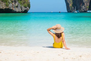 Sarı mayo ve şapkalı kadın turist, Tayland, Krabi 'deki Phi Phi Adası' ndaki Maya Körfezi plajında güneşlenen mutlu gezgin. tarihi eser, hedef Güneydoğu Asya Seyahat, tatil ve tatil konsepti