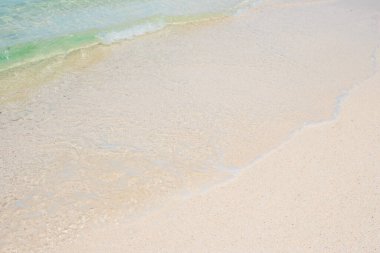 Mavi deniz suyunun yumuşak dalgası ve güzel sahilde beyaz kum. Arkaplan, duvar kağıdı ve soyut kavram