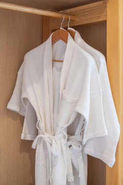 White clean bathrobe hanging in wooden wardrobe at luxury hotel or home. Relax and travel concept