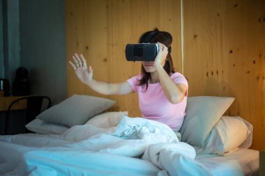Yatakta sanal gerçeklik kulaklığı kullanan genç bir kadın. VR, gelecekteki dijital teknoloji, oyun, film eğlencesi, metaevren, NFT ve 3D siber uzay kavramı