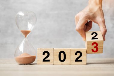 hand flipping block 2022 to 2023 text with hourglass on table. Resolution, time, plan, goal, motivation, reboot, countdown  and New Year holiday concepts