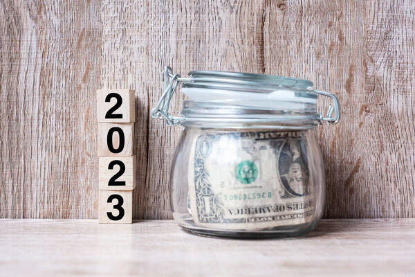 2023 Happy New Year with US dollar money glass American on wood table background. business, investment, retirement planning, finance, Saving and New Year Resolution concepts