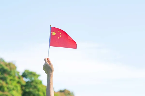 hand holding China flag on blue sky background. National Day of the People Republic of China, public Nation holiday Day and happy celebration concepts