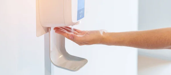 hand spray by automatic sanitizer dispenser in office or apartment. Contactless and Personal hygiene concept
