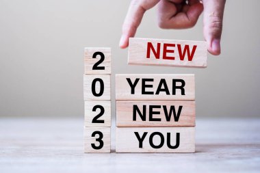 hand holding wooden block with text 2023 NEW YEAR NEW YOU on table background. Resolution, strategy, goal, business and holiday concepts clipart