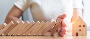 Kadın eli, tahta bloklardan düşmeyi bırak ve ev modelini koru. Kriz, Sonbahar İşletmeleri, Risk, Ekonomik durgunluk, Geliştirici, Gayrimenkul ve Gayrimenkul kavramı