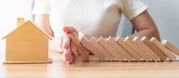 woman hand stop falling wood blocks and protect house model. Crisis, fall Business, Risk, Economic recession, Developer, Real Estate and Property concept