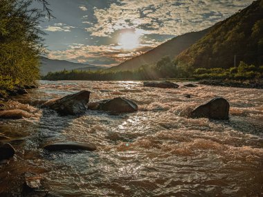 Gün batımında nehrin üzerinde güzel bulutlu bir gökyüzü. Nehrin yüksek kıyısı otlarla kaplıdır. Nehrin karşı kıyısı alçak ve üzerinde bir orman yetişiyor..