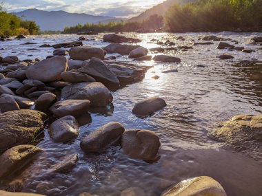 Gün batımında nehrin üzerinde güzel bulutlu bir gökyüzü. Nehrin yüksek kıyısı otlarla kaplıdır. Nehrin karşı kıyısı alçak ve üzerinde bir orman yetişiyor..