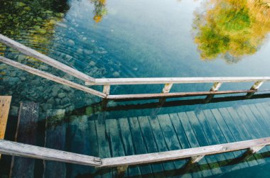 Tahta iskelesi ve su basamakları olan güzel sakin göl suyu. Şeffaf zümrüt suyu