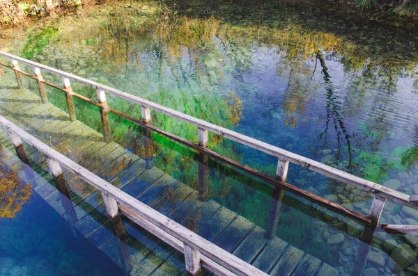 Beautiful calm water of lake with wooden pier and stairs leading in water. Transparent emerald water