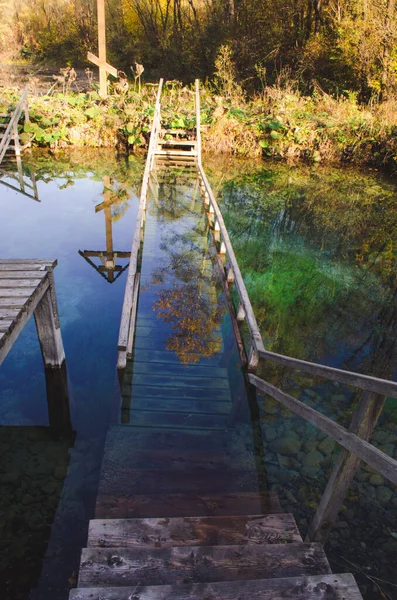 Beautiful calm water of lake with wooden pier and stairs leading in water. Transparent emerald water