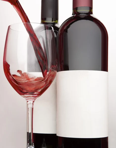 Pouring a glass of red wine and two bottles — Stock Photo, Image