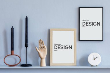 Zarif bir oturma odasının içinde, modern ev sahnelemelerinde raflarda iki tane sahte çerçeve, beyaz saat, mumlar, ahşap el, gri ahşap paneller ve zarif aksesuarlar olan şık bir ev..