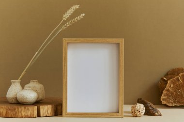 Poster çerçevesi, ahşap ve marbel gibi doğal malzemeler, kurumuş bitkiler ve kişisel aksesuarlarla süslenmiş şık iç tasarım kompozisyonu. Tarafsız ve sarı renkler, şablon.