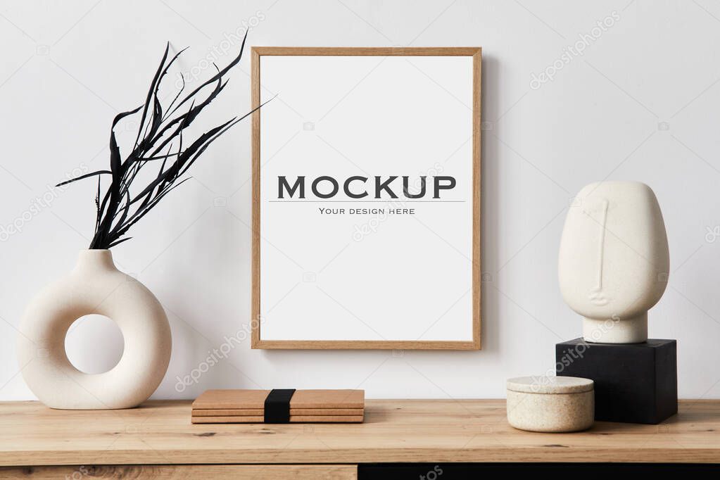 Stylish interior of living room with mock up poster frame, wooden commode, book, black leaf in ceramic vase and elegant personal accessories. Minimalist concept of home decor. Template.