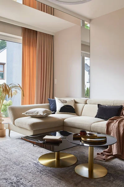 Stylish composition of living room interior with beige sofa, glass coffee table, carpet on the floor and glamorous accessories. Template.