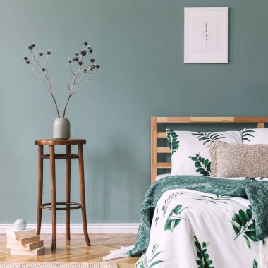 Rahat ve şık yatak odasının yaratıcı kompozisyonu poster çerçevesi, yatak, yeşil yapraklı beyaz çarşaf, halı, sehpa olarak ahşap küp ve boho aksesuarları. Okaliptüs duvarı ve parke zemin. Şablon