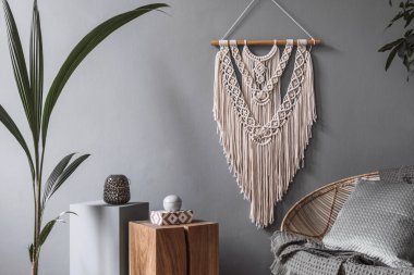 Yaratıcı ve rahat oturma odasının şık kompozisyonu Boho iç dekorasyonu ve rattan koltuğu. Gri duvarlar