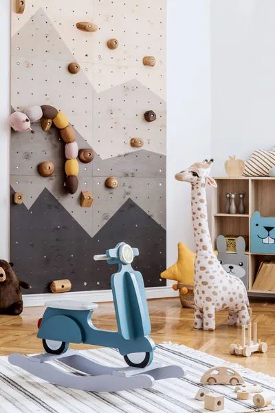 Stylish scandinavian interior design of childroom with modern climbing wall for kids, design furnitures, soft toys, teddy bear and cute children\'s accessories. Template.