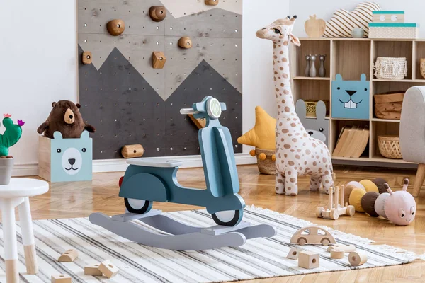 Stylish scandinavian interior design of childroom with modern climbing wall for kids, design furnitures, soft toys, teddy bear and cute children\'s accessories. Template.