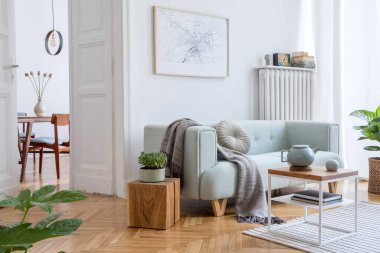 Poster çerçevesi, yeşil kanepe, ahşap mobilya, bitkiler ve aksesuarlarla süslenmiş şık ve yaratıcı oturma odası iç tasarımı. Beyaz duvarlar, parke zemin. Şablon.