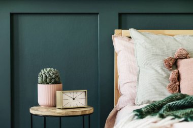 Tasarım sehpası, bitki, altın saat ve zarif kişisel aksesuarları olan şık bir yatak odası. Güzel çarşaflar, battaniye ve yastıklar. Şablon. Modern ev dekorasyonu. 