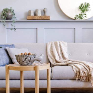  Şık gri kanepe, kahve masası, tropik bitki, ayna, dekorasyon, yastık, ekose ve zarif kişisel aksesuarları modern ev dekorunda olan İskandinav oturma odasının iç tasarımı..