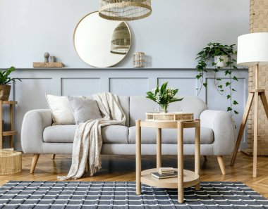 Tasarım gri kanepe, ahşap sehpa, tropikal bitkiler, raf, ayna, mobilya, ekose yastık, çaydanlık, kitap ve ev dekorunda zarif kişisel aksesuarlar ile İskandinav oturma odası.