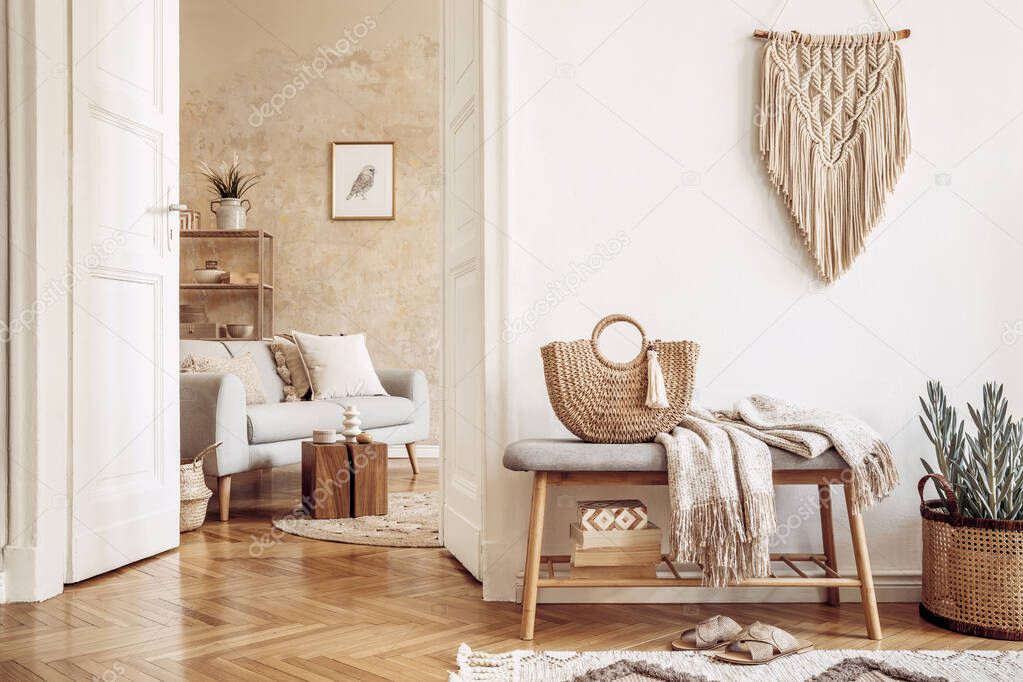 Scandinavian interior of open space with wooden bench, grey sofa, pillows, palid, picture frame, macrame, plant, books, carpet, shelf, decoration and elegant personal accessoreis in stylish home decor.