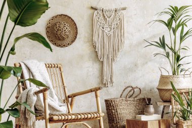 Oturma odasının iç kısmının şık ve çiçekli kompozisyonu içinde rattan koltuklar, tasarım kapları, dekorasyon, makrome ve şık ev dekorasyonu gibi pek çok tropikal bitki var..