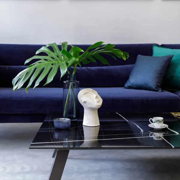 Stylish and modern living room interior with blue velvet sofa, mock up paintings, design furniture, plant, table, decoration, concrete floor, elegant personal accessories in home decor.