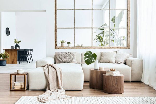 Modern interior of open space with design modular sofa, furniture, wooden coffee tables, plaid, pillows, tropical plants and elegant personal accessories in stylish home decor. Neutral living room.